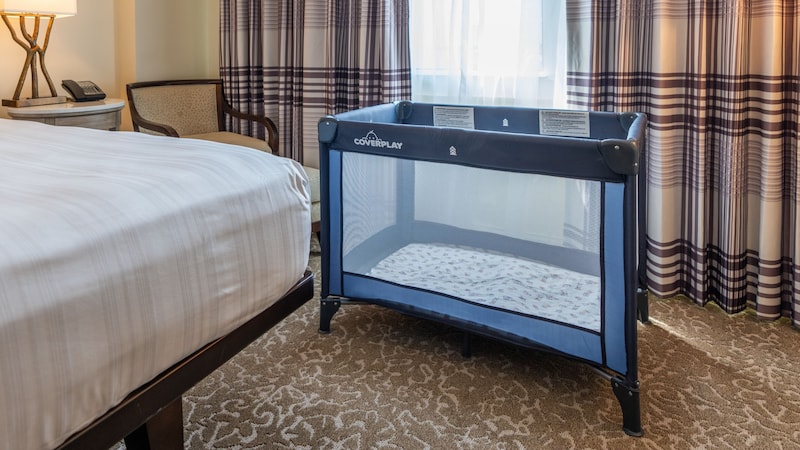  A hotel room with a crib positioned beside a bed near a curtained window