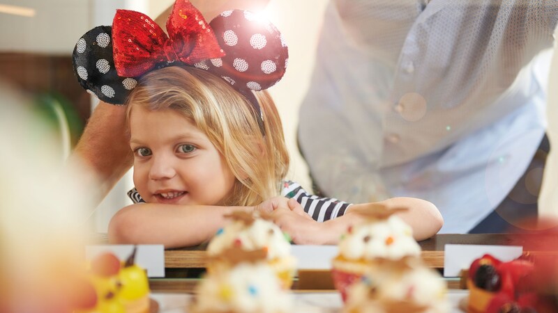  A young girl in a Minnie Mouse ear headband looking at a display of pastries