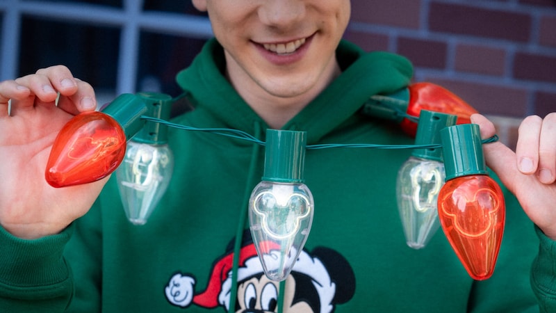 A Guest wearing a Santa Mickey Mouse hoodie while holding up a Mickey Mouse light necklace