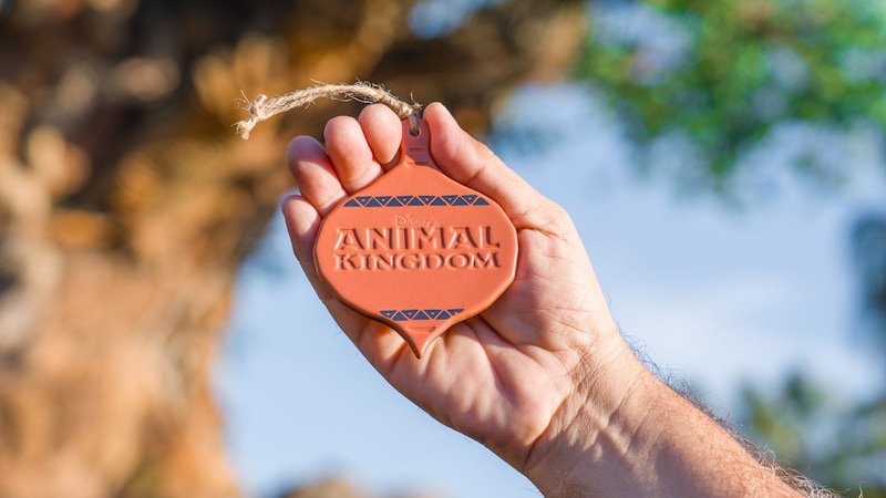 A Guest holding a Disney’s Animal Kingdom ornament near the Tree of Life