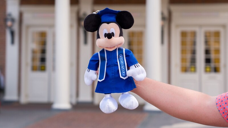A hand holding a Mickey Mouse plush dressed in a 2026 graduation outfit
