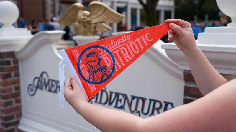 A Guest holding a patriotic pennant featuring Sam Eagle near the American Adventure at Epcot