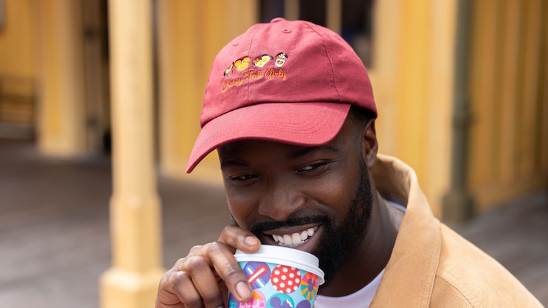 A Guest sipping from a Disney Parks cup while wearing a Disney Fall Girly embroidered hat