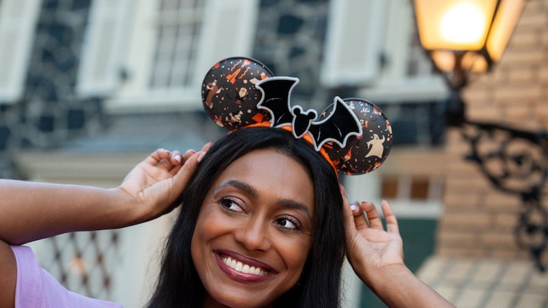 A Guest smiling while adjusting a Halloween bat Mickey Mouse ear headband