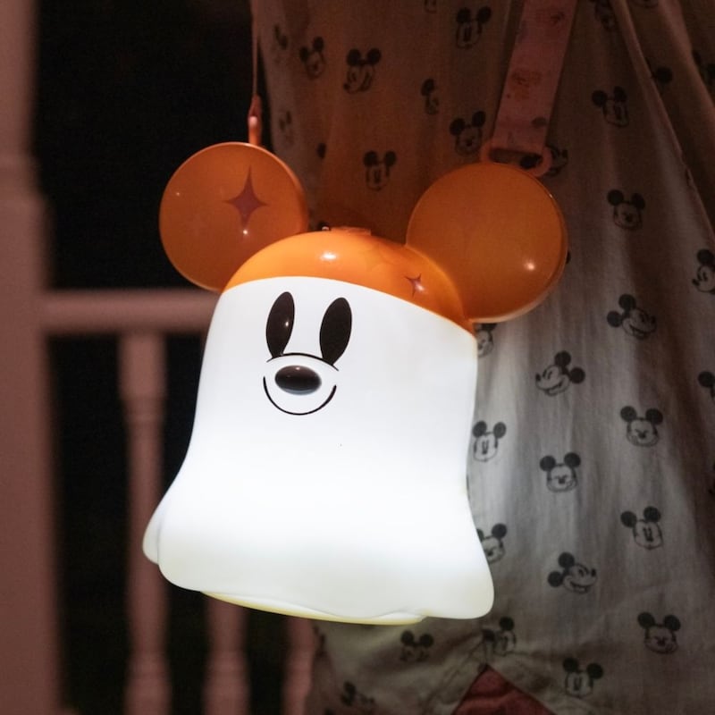 A Guest carrying a glowing Mickey Mouse ghost shaped lantern bag at night