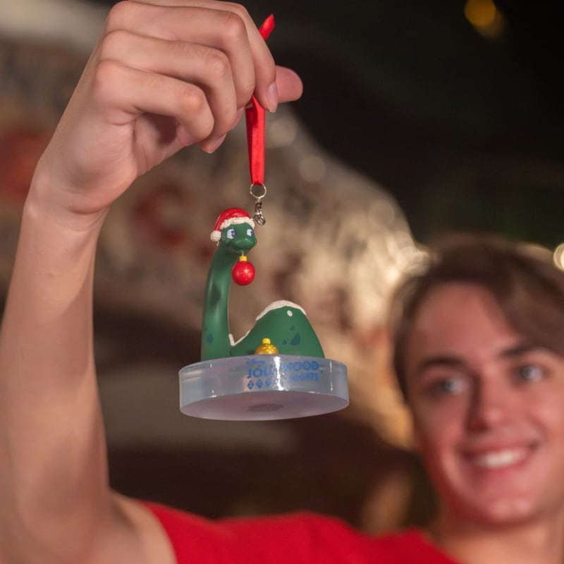 A boy holding up a holiday ornament featuring Dinosaur Gurtie wearing a Santa hat