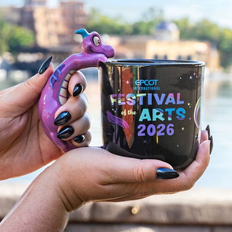 Hands holding a Figment themed Epcot International Festival of the Arts 2026 mug