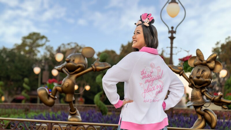 The back of a Guest standing between bronze statues of Mickey Mouse and Minnie Mouse while wearing a Walt Disney World Resort long sleeve shirt and a Mickey Mouse and Minnie Mouse ear headband