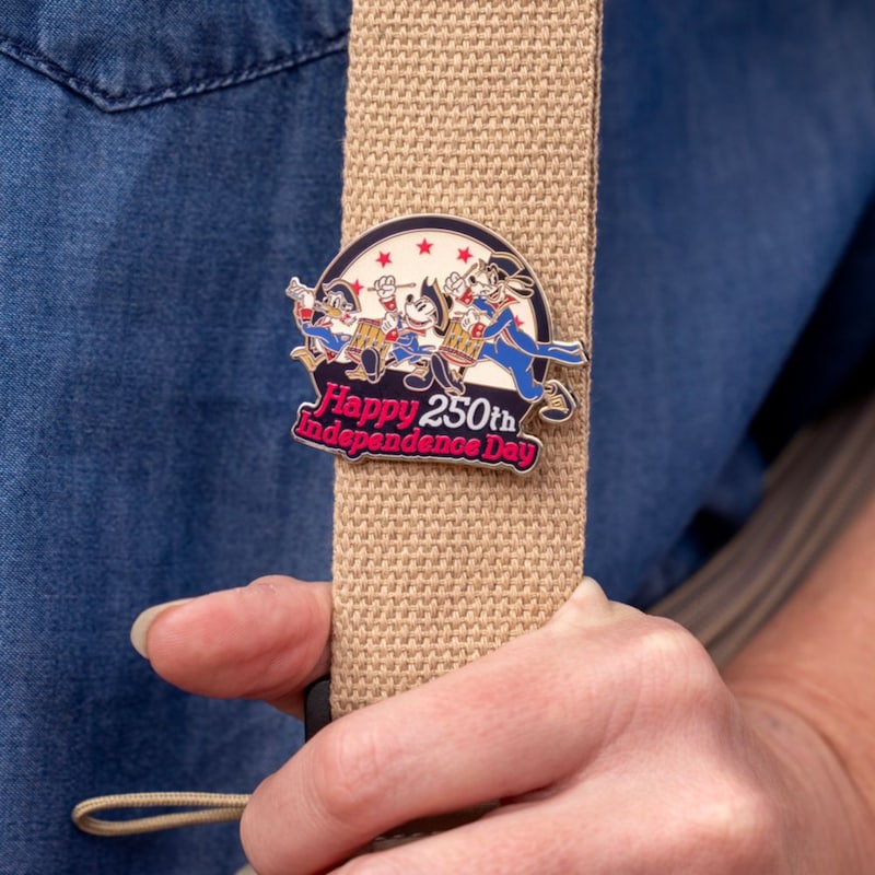 A Guest holding a bag with a Disney pin that says ‘Happy 250th Independence Day’