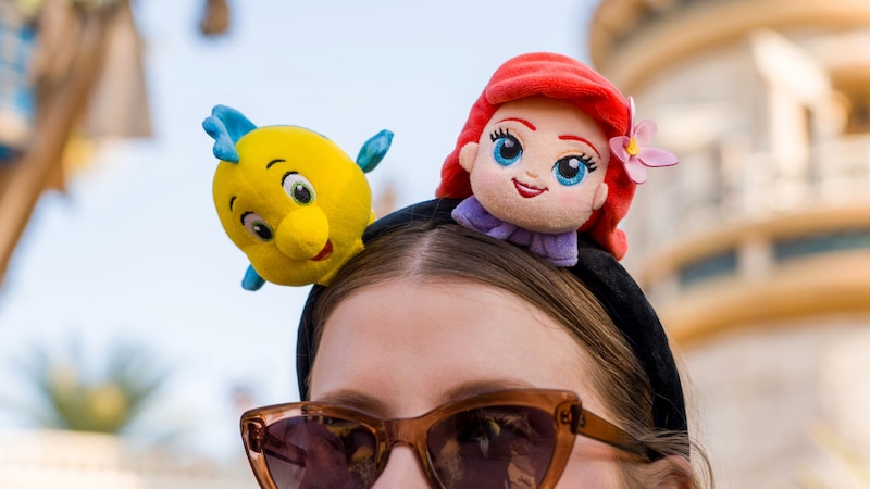 A Guest wearing sunglasses and a Minnie Mouse ear headband featuring Flounder and Ariel