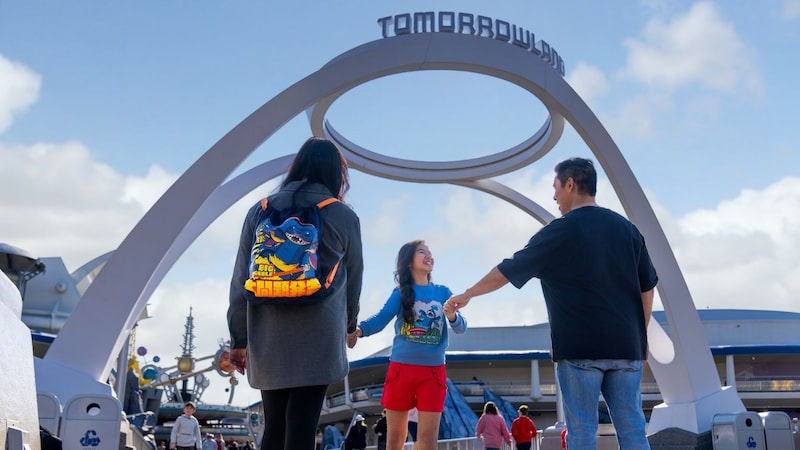 A child holding hands with 2 adults as they walk toward Tomorrowland