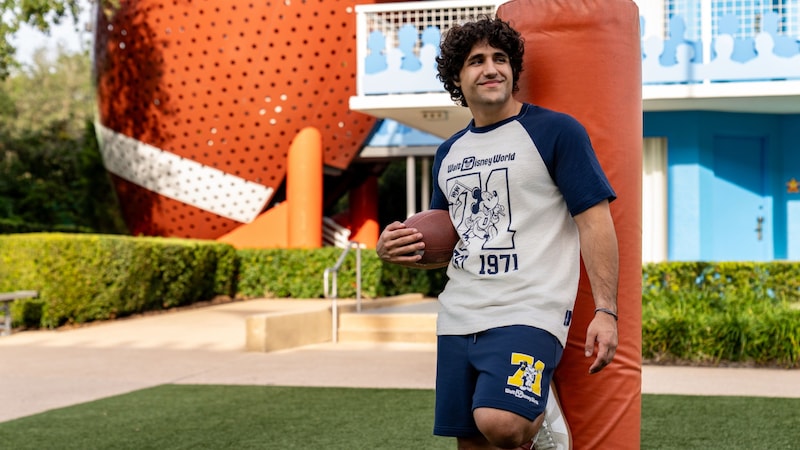 A Guest holding a football while wearing a Walt Disney World 1971 baseball T shirt and athletic shorts