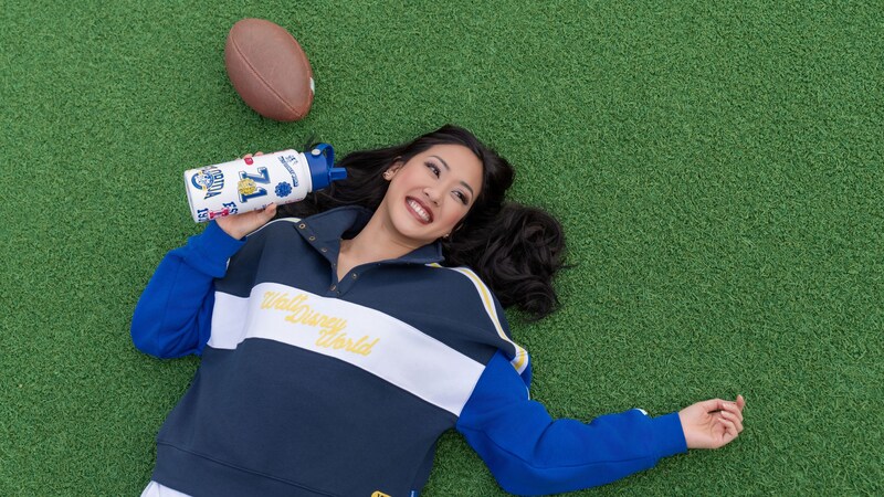 A Guest lying on the grass while wearing a Walt Disney World pullover and holding a water bottle with stickers