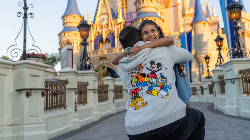 A father hugging his daughter while wearing a hoodie featuring multiple Disney characters