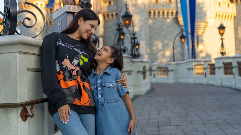 A mother hugging her daughter near Cinderella Castle while wearing a sweatshirt featuring Goofy
