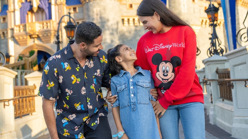 A family of 3 standing near Cinderella Castle while wearing Disney merchandise