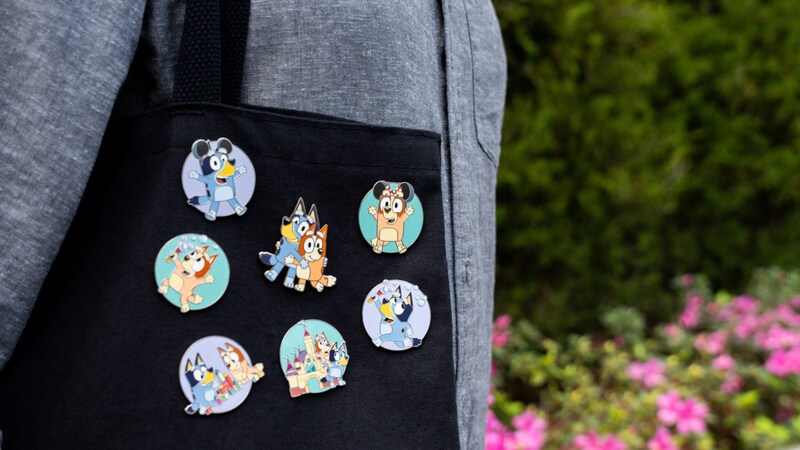 A Guest holding a tote bag with 7 pins featuring Bluey and Bingo