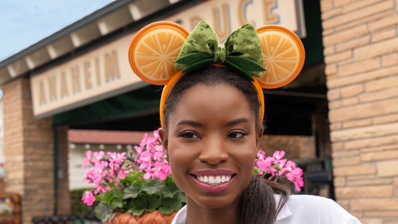 A smiling Guest wearing a fruit themed Minnie Mouse ear headband at Anaheim Produce at Disney's Hollywood Studios theme park