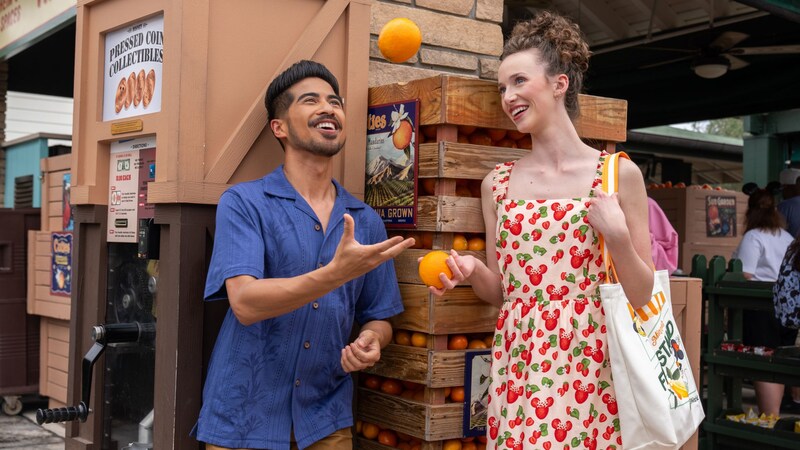 Two Guests standing together while one tosses an orange in the air outside of Anaheim Produce at Disney's Hollywood Studios theme park