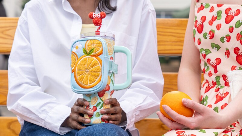Two Guests with fruit themed Disney merchandise sitting on a bench outside of Anaheim Produce at Disney's Hollywood Studios theme park
