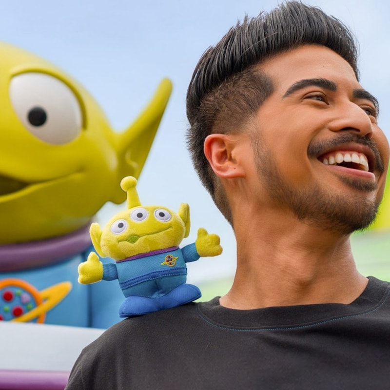 A Guest in a black T shirt with a Toy Story Alien plush on his shoulder in front of Alien Swirling Saucers