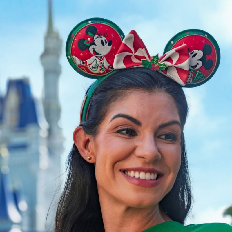 A woman wearing a holiday themed Minnie Mouse ear headband near Cinderella Castle