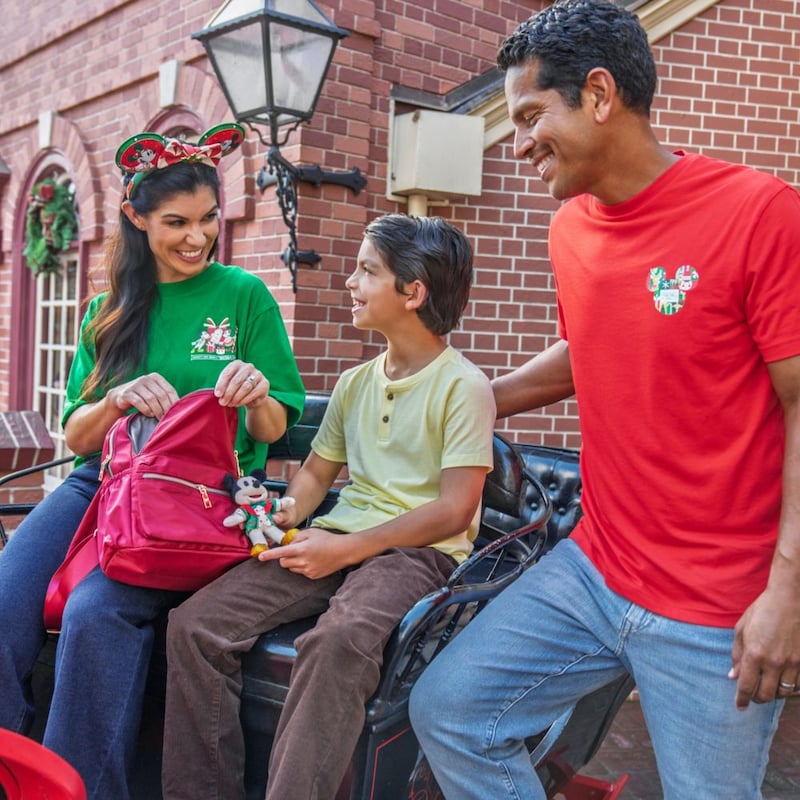 A family of 3 sitting together and wearing merchandise from the Disney Holiday Collection