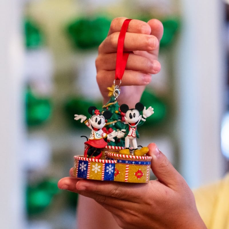 A boy holding up an ornament featuring Mickey Mouse and Minnie Mouse