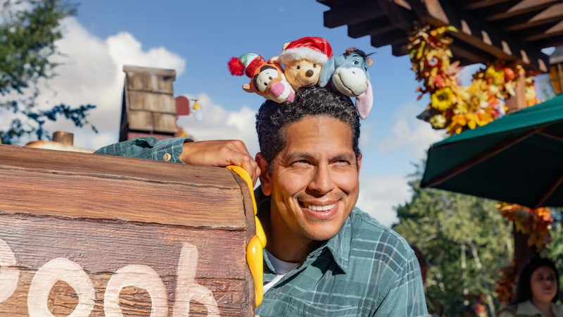A man smiling with Winnie the Pooh, Tigger and Eeyore plush toys balancing on his head