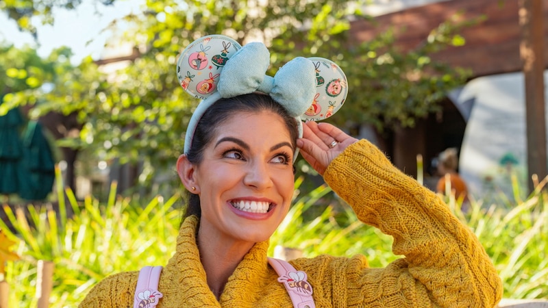 A woman smiling while wearing a Minnie Mouse ear headband decorated with Winnie the Pooh