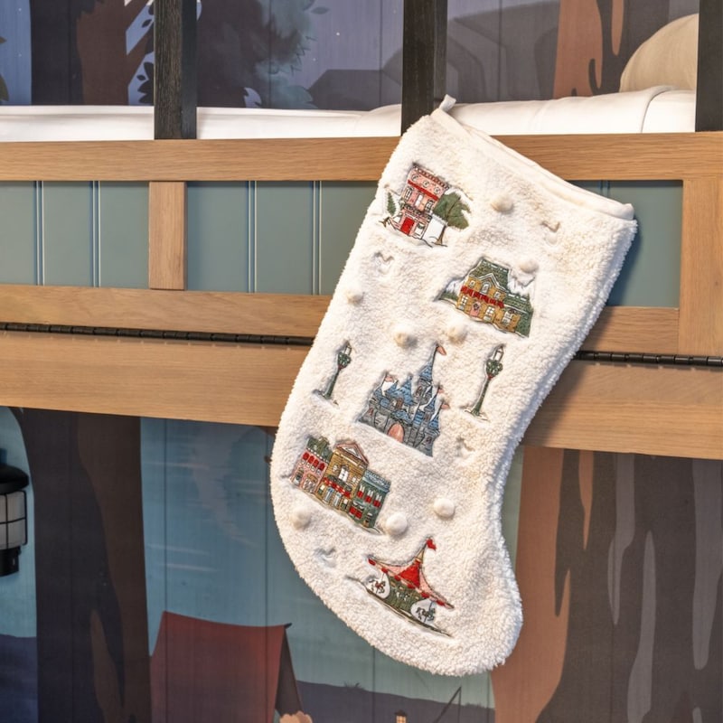 An embroidered holiday stocking featuring Disney parks icons hanging on a bunk bed