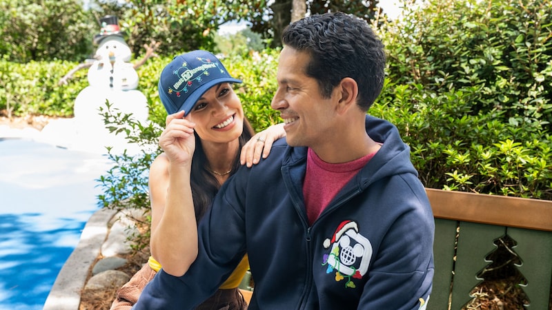 A couple in holiday themed Walt Disney World holiday merchandise sitting on a bench together