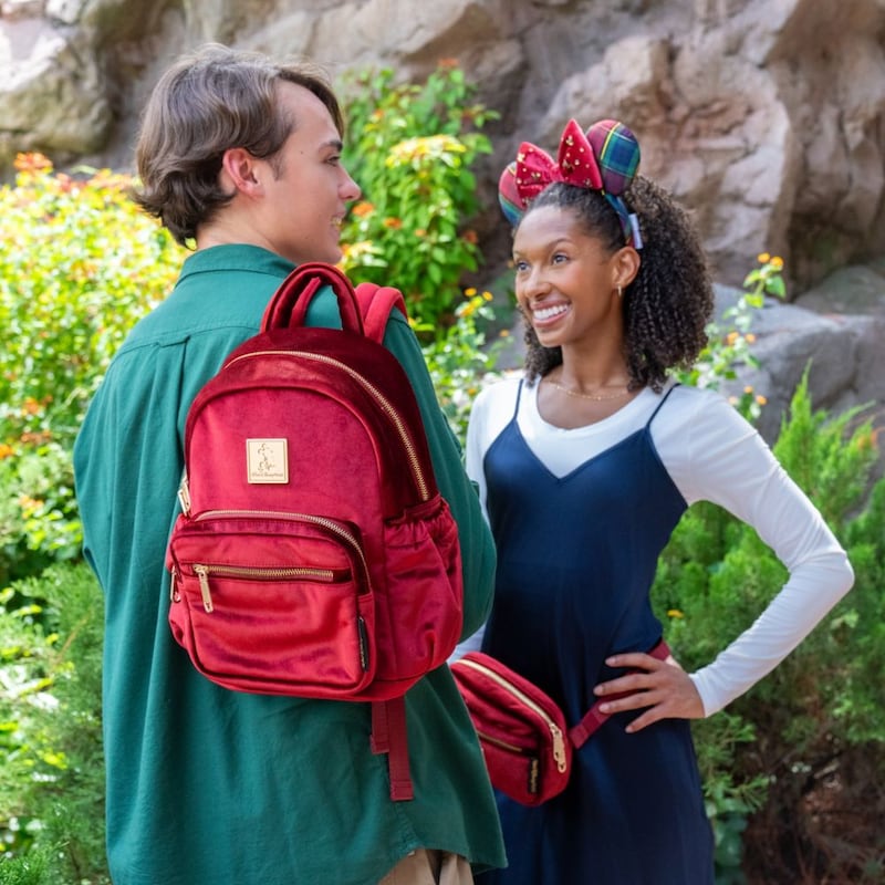 2 adults wearing Walt Disney World merchandise, one with a backpack and the other with a Minnie Mouse headband and hip pack