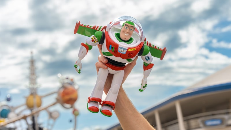 A hand holding a Buzz Lightyear toy wearing holiday colored armor near the Astro Orbiter and the Monorail