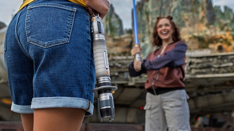 A woman holding an illuminated lightsaber facing another person with a lightsaber hilt