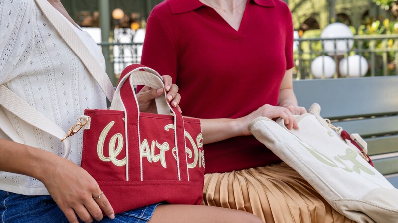 Two women holding canvas tote bags embroidered with the Walt Disney World script logos