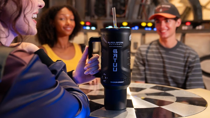 A woman holding a Batuu travel mug while sitting with 2 other Guests