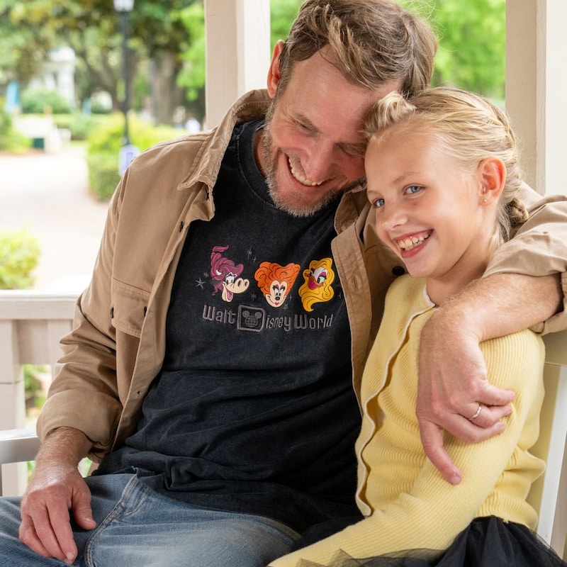A father and daughter sitting together on a bench beside a waterfront area