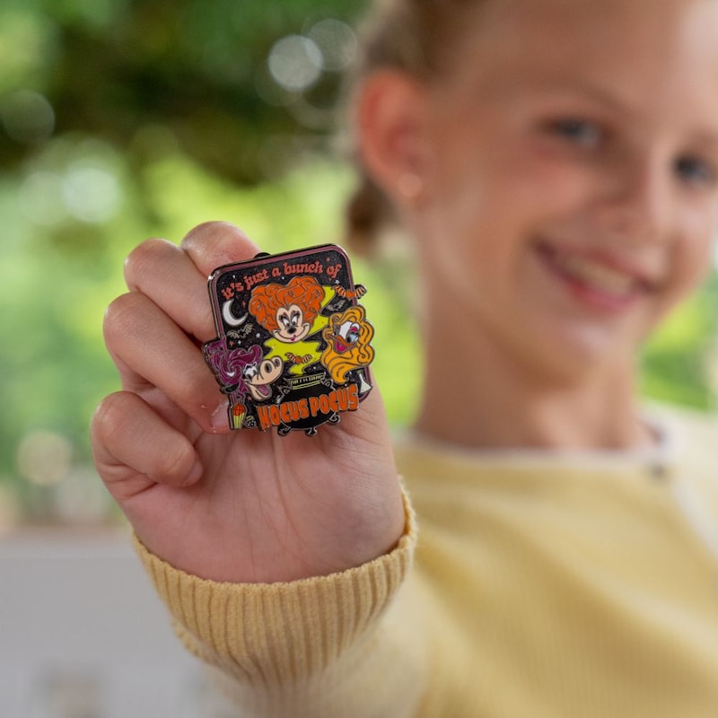 A child smiles while holding a Hocus Pocus themed pin
