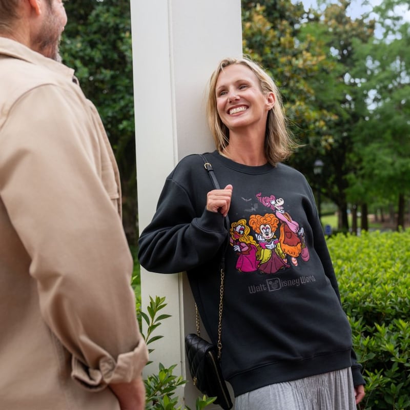 A Guest in a Halloween themed Walt Disney World sweatshirt chatting with another Guest near landscaped greenery