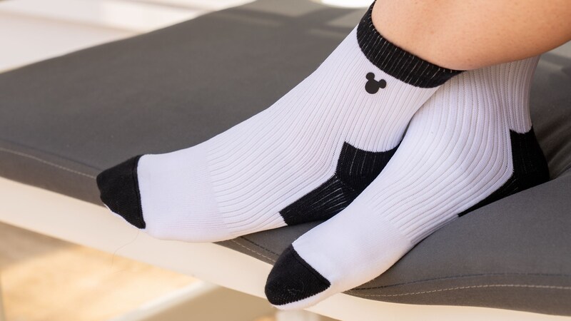 A Guest wearing a pair of crew socks with a Mickey Mouse icon on a cushioned chair