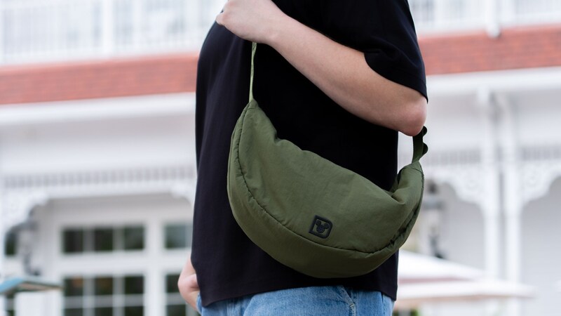 A Guest wearing a Walt Disney World crossbody bag outside a Resort hotel building