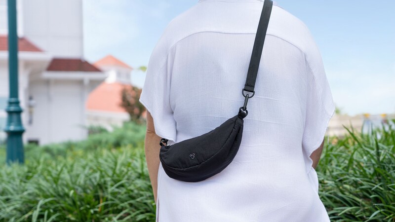 A Guest wearing a Mickey Mouse crossbody belt bag over a shirt near landscaped greenery