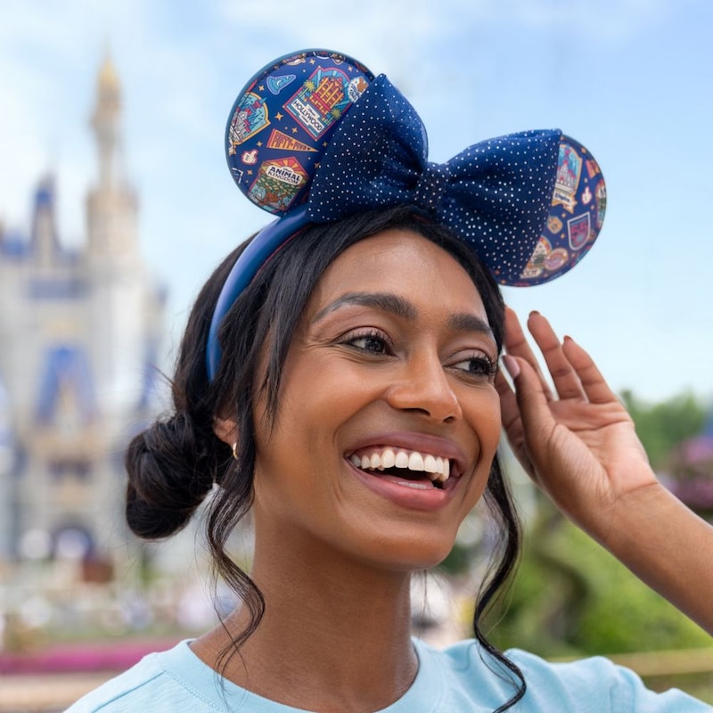 A Guest wearing a Mickey Mouse ear headband featuring Walt Disney World attractions in front of Cinderella Castle