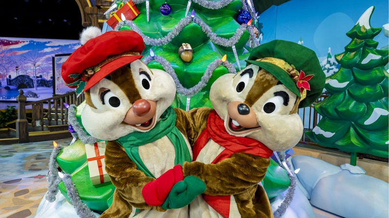 Chip and Dale wearing Christmas outfits and hugging in front of the Christmas tree at  Holiday Fun with Santa and Friends