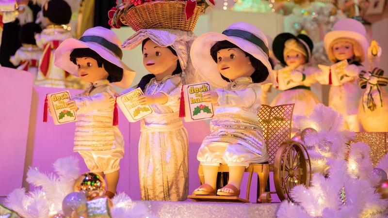 3 animatronic dolls hold books that read ‘deck the halls’ on ‘it’s a small world’ in Magic Kingdom park