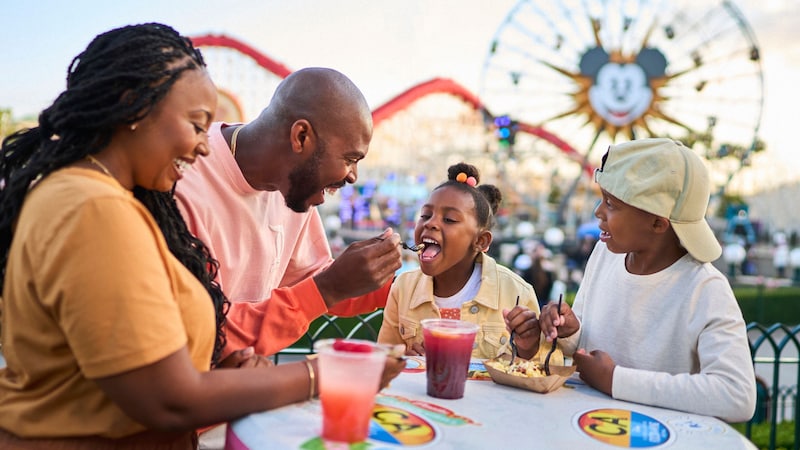 A family enjoys some food and beverages at an outdoor table at Disney California Adventure Park