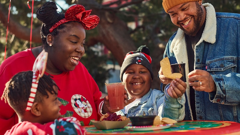 A family sitting at a table, wearing Christmas themed outfits eating and drinking holiday food and drinks