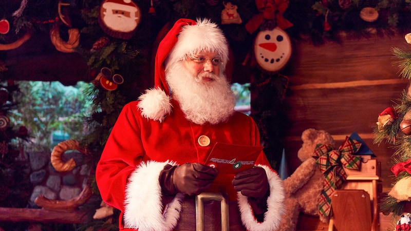 Santa Claus holding a letter in a cabin filled with Christmas decorations