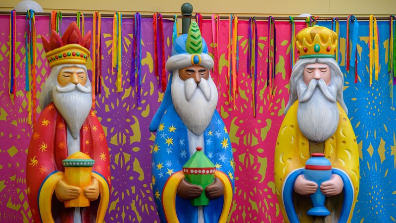 Three Kings Day figures holding gifts in front of decorations